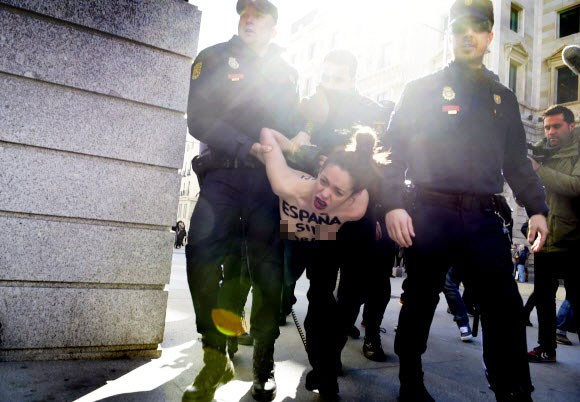 24일(현지시간) 스페인 마드리드시 의회 청사 앞에서 가슴에 “재갈 없는 스페인(을 원한다)”(Spain without Mordaza)이라는 메시지를 적은 여성 페미니스트 단체 페멘(Femen) 소속 회원이 경찰들에게 체포된 채 끌려가고 있다.  ⓒAFPBBNews=News1