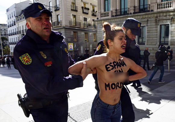 24일(현지시간) 스페인 마드리드시 의회 청사 앞에서 가슴에 “재갈 없는 스페인(을 원한다)”(Spain without Mordaza)이라는 메시지를 적은 여성 페미니스트 단체 페멘(Femen) 소속 회원이 경찰들에게 체포된 채 끌려가고 있다.  ⓒAFPBBNews=News1