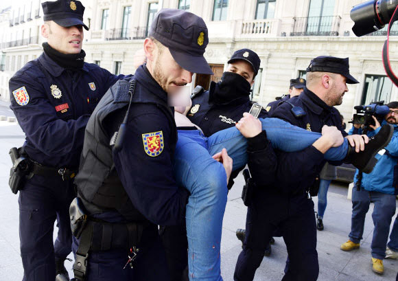 24일(현지시간) 스페인 마드리드시 의회 청사 앞에서 가슴에 “재갈 없는 스페인(을 원한다)”(Spain without Mordaza)이라는 메시지를 적은 여성 페미니스트 단체 페멘(Femen) 소속 회원이 경찰들에게 체포된 채 끌려가고 있다.  ⓒAFPBBNews=News1