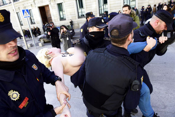 24일(현지시간) 스페인 마드리드시 의회 청사 앞에서 가슴에 “재갈 없는 스페인(을 원한다)”(Spain without Mordaza)이라는 메시지를 적은 여성 페미니스트 단체 페멘(Femen) 소속 회원이 경찰들에게 체포된 채 끌려가고 있다.  ⓒAFPBBNews=News1