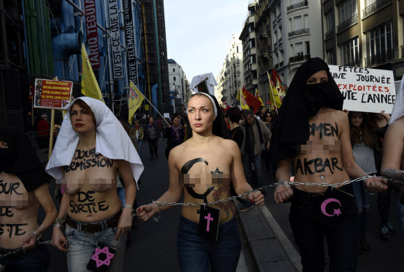 8일(현지시간) 프랑스 파리에서 ‘세계 여성의 날’을 맞아 퍼레이드가 열린 가운데 국제여성인권단체 페멘(FEMEN)의 리더 인나 셰브첸코(가운데)와 회원들이 상의를 탈의한 채 체인에 손을 묶고 행진에 참여하고 있다. ⓒAFPBBNews=News1