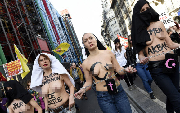 8일(현지시간) 프랑스 파리에서 ‘세계 여성의 날’을 맞아 퍼레이드가 열린 가운데 국제여성인권단체 페멘(FEMEN)의 리더 인나 셰브첸코(가운데)와 회원들이 상의를 탈의한 채 체인에 손을 묶고 행진에 참여하고 있다. ⓒAFPBBNews=News1