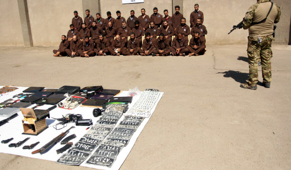 16일(현지시간) 이라크 수도 바그다드에 위치한 이라크 국가정보원 청사 앞에 이라크 정부군이 이슬람 수니파 무장단체 ‘이슬람국가’(IS) 대원으로 추정되는 31명의 인질을 포위하고 있다. 사진은 IS 대원 31명과 그들이 사용한 무기를 압수한 모습.  ⓒAFPBBNews=News1