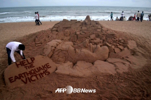 인도의 모래 조각가 수다르산 펫낵이 25일(현지시간) 인도 북동부의 푸리 해변에서 네팔 대지진 희생자를 도와달라는 문구와 함께 지진 피해를 형상화한 모래 조각을 만들고 있다. ⓒ AFPBBNews=News1