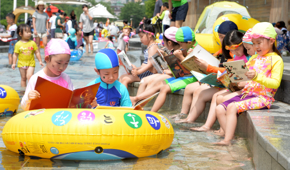 28일 서울 송파구 성내천 물놀이장을 찾은 어린이들이 인근에 마련된 ‘피서지 문고’에서 책을 빌려 물속에서 책을 읽고 있다.  박지환 기자 popocar@seoul.co.kr
