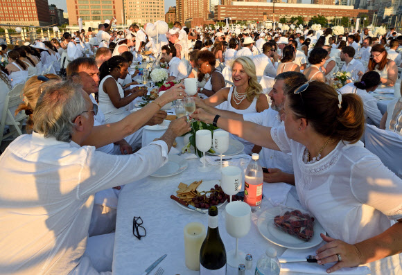 28일(현지시간) 뉴욕 피어 26에서 연례행사 디네 앙 블랑(Diner en Blanc) 참가자들이 저녁식사 전에 건배를 하고 있다. 약 5,000명의 사람들이 흰색 옷을 입고 자신의 디너와 테이블을 가져와 참여하고 있다.  ⓒ AFPBBNews=News1