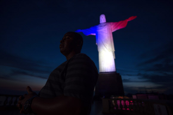 한 남자가 프랑스 수도에서 테러리스트들의 공격으로 적어도 129명이 사망한 다음날인 14일 희생자를 애도하는 의미로 프랑스 국기를 상징하는 파란색, 흰색, 붉은색 조명을 비춘 브라질 거대 예수상 앞에서 기도를 드리고 있다. ⓒ AFPBBNews=News1