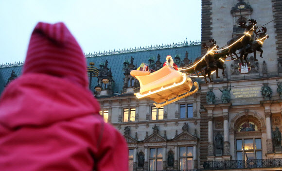 22일(현지시간) 독일 함부르크의 타운홀 앞에 산타클로스가 루돌프가 끄는 썰매를 타고 하늘을 나는  동화 같은 모습을 재현해 사람들의 시선을 끈다. ⓒ AFPBBNews=News1