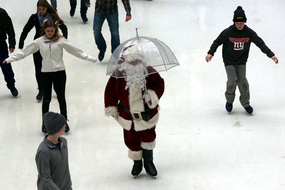 22일(현지시간) 미국 뉴욕 록펠러 센터의 스케이트장에 한 손에 투명한 비닐우산을 들고 등장한 산타클로스가 사람들 사이를 가로지르며 스케이트를 타고 있다. ⓒ AFPBBNews=News1