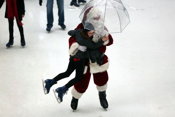 22일(현지시간) 미국 뉴욕 록펠러 센터의 스케이트장에 한 손에 투명한 비닐우산을 들고 등장한 산타클로스가 스케이트를 타던 소녀를 번쩍 들어 올리고 있다. ⓒ AFPBBNews=News1