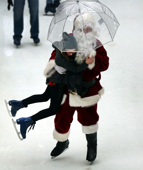 22일(현지시간) 미국 뉴욕 록펠러 센터의 스케이트장에 한 손에 투명한 비닐우산을 들고 등장한 산타클로스가 스케이트를 타던 소녀를 번쩍 들어 올리고 있다. ⓒ AFPBBNews=News1