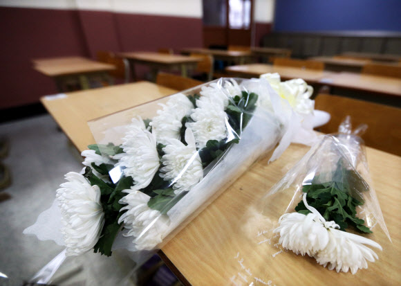 학교폭력으로 자살한 학생의 책상위에 급우들의 애도하는 마음이 담긴 꽃다발이 놓여 있다.