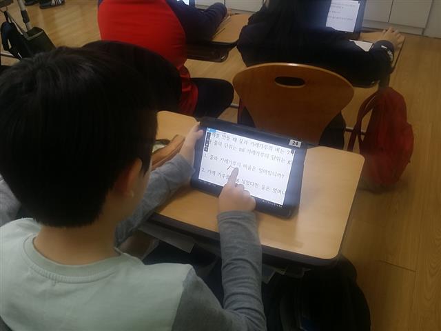 스마트스쿨인 한 초등학교에서 학생이 책상 위에 교과서와 노트 대신 태블릿PC를 펴놓고 칠판 대신 전자패널과 펜으로 가르치는 선생님의 수업을 듣고 있다.  세종시교육청 제공