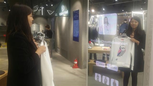 15일 서울 강남구 코엑스몰 여성복 매장에서 한 여성이 옷을 입은 모습을 찍어 비교해 주는 ‘스마트거울’에 티셔츠를 비춰 보고 있다.