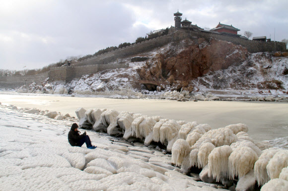 지난 주말 중국 전역을 휩쓴 한파가 진정되기 시작한 25일 동부 산둥성 펑라이 지역을 찾은 한 남성이 휴대전화로 바닷가에 얼어붙은 바위 사진을 찍고 있다. 펑라이 AFP 연합뉴스