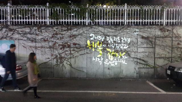 2015년 11월 저녁 8시 서울 동작구 노량진2동 동작구청 뒷길 담벼락에 설치된 응원의 벽(빔프로젝터로 ‘위로 문구’ 게시) 앞을 시민들이 지나가고 있다.