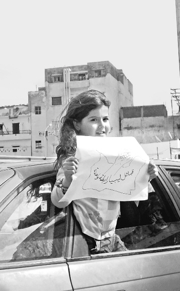 리비아의 어린이가 자동차를 탄 채 ‘리비아 국민이 단결했다’고 쓰인 글과 주먹이 그려진 종이를 들고 있다.  문학동네 제공
