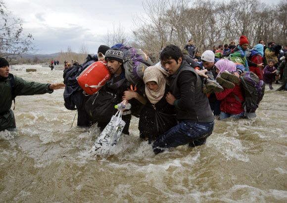 14일(현지시간) 그리스 북부 이도메니 부근에서 이민자들이 마케도니아로 향하기 위해 로프를 이용해 강을 건너고 있다. 이도메니 등지의 난민 캠프를 떠난 이민자 수백명이 이날 국경을 넘어 마케도니아 영토로 진입한 것으로 알려졌다.  AP 연합뉴스