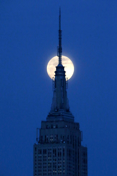 22일(현지시간) 밤 미국 뉴욕 맨해튼의 상징인 엠파이어 스테이트 빌딩 맨 꼭대기에 그림 같은 보름달이 걸려 있다. 뉴저지 호보켄의 허드슨 강가에서 바라 본 모습이다. AP 연합뉴스