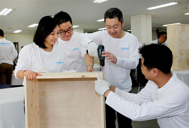 박정원(오른쪽 두 번째) 두산그룹 회장이 지난 15일 ‘두산인 봉사의 날’ 행사를 맞아 서울 중구 명동 가톨릭회관에서 저소득층 가정에 전달될 가구를 만들기 위해 전기 드릴로 못을 박고 있다. 두산 제공