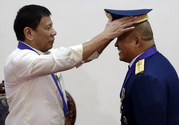 로드리고 두테르테 필리핀 대통령(왼쪽)이 1일(현지시간) 마닐라에서 로널드 델라로사 신임 경찰청장에게 모자를 씌워주고 있다. AP 연합뉴스