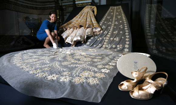 영국 엘리자베스 2세 여왕의 90번째 생일을 맞이해 영국 런던 버킹엄궁에서 열리는 ‘패션으로 본 통치: 스타일 90년(Fashioning a Reign: 90 Years of Style)’ 전시회에서 21일(현지시간) 이 전시회의 큐레이터가 여왕이 입었던 드레스들을 소개하고 있다.  AP 연합뉴스