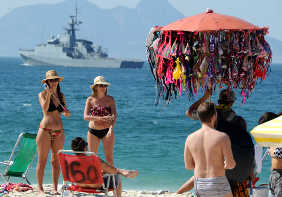 24일(현지시간) 브라질 리우데자네이루 해안에서 브라질군 경비정이 리우 올림픽에 대비해 순찰을 하는 가운데 시민들이 코파카바나 해변에서 해수욕을 즐기고 있다. AFP 연합뉴스