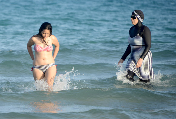 한 튀니지 여성(오른쪽)이 16일(현지시간) 튀니지의 수도 튀니스 북동쪽 반자르트 근처 Ghar El Melh 해변에서 이슬람교 여성들을 위해 디자인된 전신수영복인 ‘부르키니(burkini)’ 입고 있다. AFP 연합뉴스