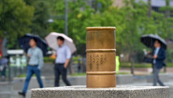여름의 끝과 가을의 시작을 알리는 비가 내린 31일 서울 광화문광장에 놓인 측우기 모형 너머로 우산을 쓴 시민들이 걸어가고 있다.  손형준 기자 boltagoo@seoul.co.kr