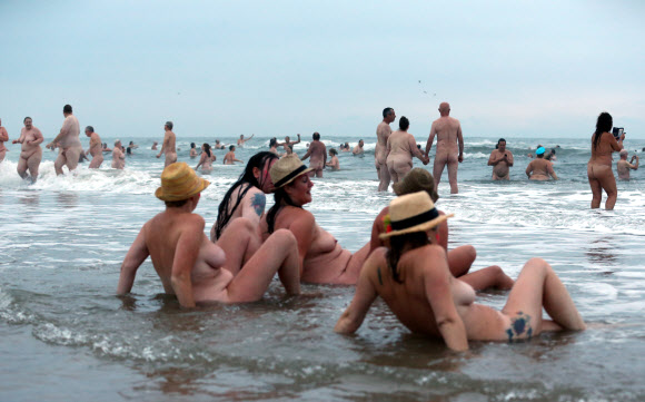25일(현지시간) 나체주의자들이 잉글랜드 북동쪽에 위치한 노섬벌랜드의 드루리지 베이에서 연례행사인 ‘노스 이스트 알몸으로 수영하기(North East Skinny Dip)’에 참가해 누드로 바닷가에서 한가한 시간을 보내고 있다.  AFP 연합뉴스