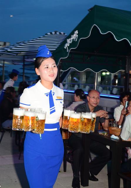 지난 8월 12일 열린 북한 평양 대동강맥주축제에서 한 직원이 대동강맥주잔을 양손 가득 들고 걸어가고 있다. 연합뉴스