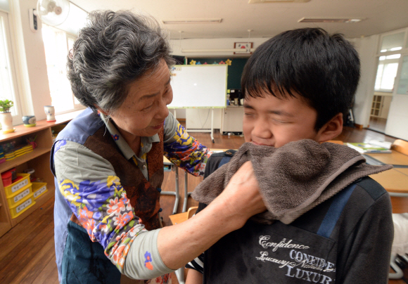 구산초등학교 1학년 교실에서 이명개 할머니가 같은 반 동기 배건휘 어린이의 얼굴을 씻기고 있다.