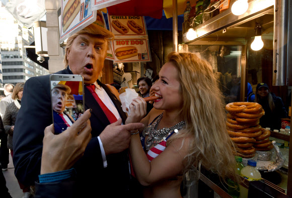 미국 공화당 대선후보 도널드 트럼프의 성추문을 풍자해 25일(현지시간) 미국 뉴욕에서 가짜 트럼프와 비키니를 입은 여성이 소시지를 들고 퍼포먼스를 하고 있다. AFP 연합뉴스