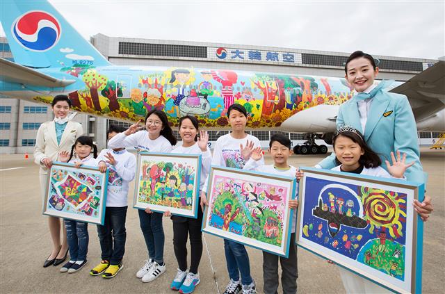 지난 29일 서울 강서구 공항동 대한항공 본사 격납고에서 열린 ‘제8회 내가 그린 예쁜 비행기’ 그림대회 시상식에 참가한 어린이들이 1등 작품이 그려진 B777-300ER 항공기 앞에서 한 손에 수상작을 든 채 미소를 짓고 있다. 대한항공 제공