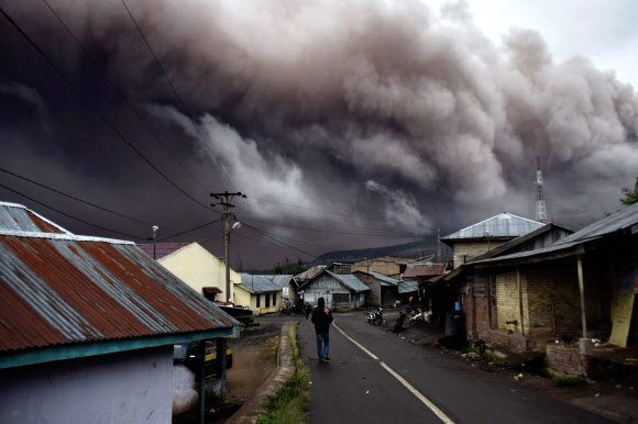 1일(현지시간) 인도네시아 수마트라섬의 시나붕 화산이 분화, 화산재를 뿜어내고 있는 가운데 한 남성이 길을 걸어가고 있다.
 ‘불의 고리’에 속한 시나붕 화산은 지난 5월에도 화산이 분출해 주민 6명이 사망했었다. AFP 연합뉴스
