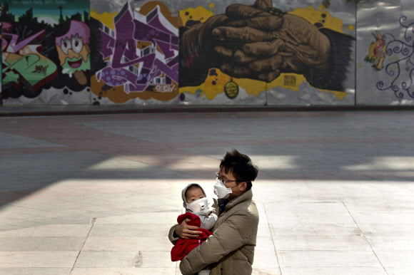 5일(현지시간) 중국 베이징에서 스모그 악화 등 심각한 공기오염으로 아이를 안은 남성이 아이와 나란히 마스크를 쓰고 거리를 지나고 있다.  AP 연합뉴스