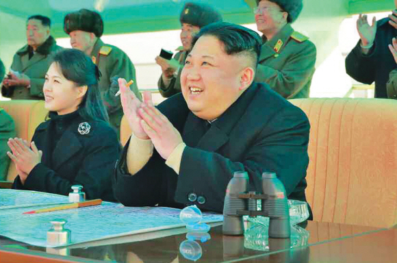 지난 4일 북한 김정은(오른쪽) 노동당 위원장이 부인 리설주와 함께 군의 전투비행술 경기대회를 참관하며 피우던 담배를 손에 낀 채 박수를 치고 있다. 2016-12-4 연합뉴스