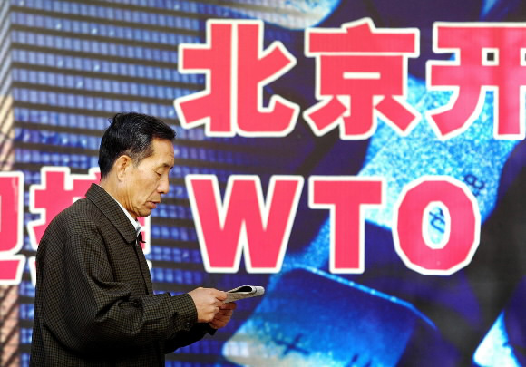 중국의 세계무역기구(WTO) 가입을 한 달 앞둔 2001년 11월 11일 한 중국인이 신문을 보며 베이징 거리에 세워진 ‘중국 WTO 가입’ 홍보판 옆을 걸어가고 있다. 서울신문 포토라이브러리. 