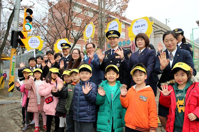 지난해 12월 5일 경기 안산 와동초등학교에서 열린 현대차 기부 드라이빙 캠페인에 참석한 경찰 관계자 및 어린이들이 노란색 안전 신호등 앞에서 손을 들어 보이고 있다. 현대차 제공