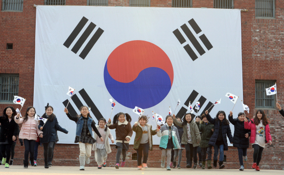 3·1절을 하루 앞둔 28일 서울 서대문구 서대문형무소역사관을 찾은 아이들이 대형 태극기 앞에서 소형 태극기를 흔들며 활짝 웃고 있다. 도준석 기자 pado@seoul.co.kr