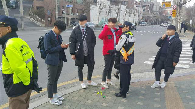 경찰관과 학부모, 지역 주민으로 이뤄진 ‘112 청소년 사랑회’ 회원들이 22일 서울 동대문구 휘경동의 한 대로변에서 아이들에게 금연 지도를 하고 있다. 바닥에는 학생들의 주머니에서 나온 라이터들.