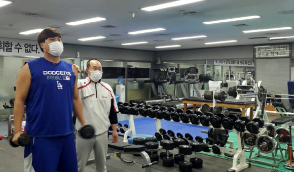 김용일 LG 트레이닝 코치가 지난해 12월 서울 잠실구장 LG 트레이닝실에서 류현진과 나란히 독감 마스크를 쓰고 그의 재활 훈련을 돕고 있다.  류현진은 독감에 걸려 병원에서 링거를 맞은 다음 날 마스크를 쓰고 나타나 훈련 프로그램을 소화했을 정도로 독하게 훈련했다고 한다.  김용일 코치 제공=연합뉴스