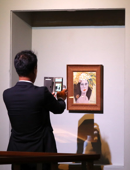 18일 오전 경기도 과천시 국립현대미술관에서 열린 고 천경자 화백 미인도 언론공개 행사에서 한 기자가 미인도를 촬영하고 있다. 국립현대미술관은 이날 언론 공개를 시작으로 19일부터 과천관에서 열리는 ’소장품전: 균열’을 통해 미인도를 일반 공개한다.  미인도 위작 논란과 관련해 검찰은 지난해 12월 미인도가 진품이라고 발표했지만 유족측은 이에 맞서 항고한 상태다.  연합뉴스