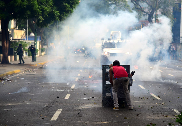 19일(현지시간) 수도 카라카스의 시위대원이 경찰 방패 뒤에 숨어 있는 모습. 시위대와 경찰의 충돌이 격화되면서 군인과 학생 등 최소 3명이 사망했다.  카라카스 AFP 연합뉴스