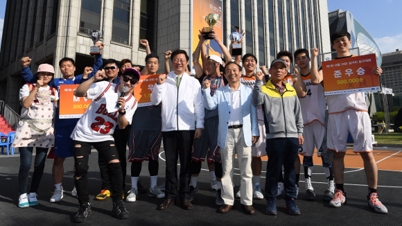 이경형(앞줄 오른쪽 두 번째) 서울신문 주필과 정창수(세 번째) 서울시체육회 사무처장, 최승대(오른쪽 모자 쓴 사람) 서울시 체육진흥과장이 지난 22일 서울 중구 서울신문사 앞 서울마당에서 열린 ‘제1회 서울 길거리 농구대회’의 우승(피데스)·준우승(CJ드림스)팀과 함께 파이팅을 외치고 있다.  박지환 기자 popocar@seoul.co.kr