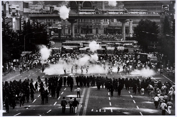 대한민국역사박물관이 민주화 30주년을 맞아 6월 민주항쟁 관련 자료를 선보이는 사진전 ‘1987년을 돌아보다’를 오는 10일부터 8월 27일까지 야외 역사마당에서 연다고 9일 전했다.이번 전시에는 1987년 1월 벌어진 박종철 고문치사 사건부터 수많은 사람이 거리로 나와 직선제 개헌과 독재정권 타도를 외친 6월 민주항쟁, 그해 12월 개헌으로 치러진 대통령 선거까지 30년 전 모습을 담은 사진 30여 점이 나온다. 사진은 민주화를 요구하는 학생 시위대와 진압하는 경찰, 서울역 앞, 1987년 구와바라 시세이 작품. 2017.6.9 [대한민국역사박물관 제공=연합뉴스