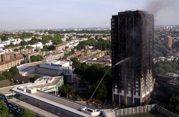 영국 런던 서부 노스켄싱턴의 24층 아파트 그렌펠 타워에서 지난 14일 발생한 화재로 최소 12명이 사망한 가운데 15일(현지시간) 화재 진압에 나선 런던 소방관들이 전소돼 검게 그을린 그렌펠 타워에 물을 뿌리고 있다. 런던 AP 연합뉴스