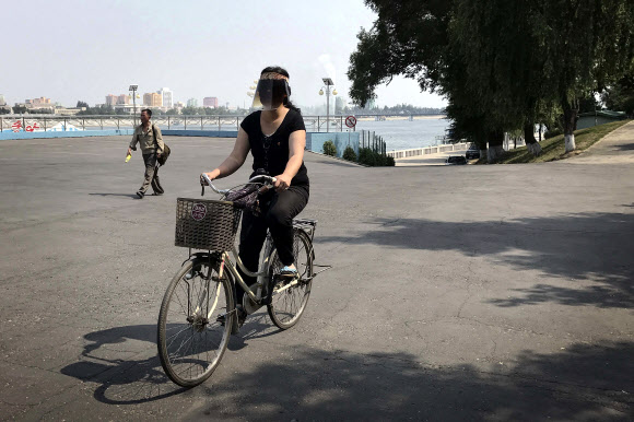 18일 북한 평양의 대동강 강둑에서 한 여성이 자전거를 타고 있다. AP 연합뉴스
