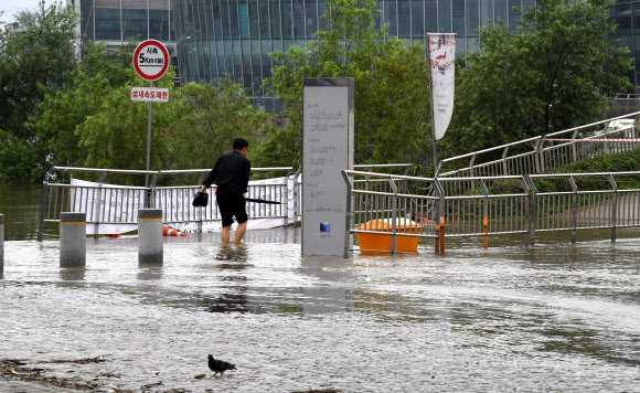 중부지방 호우로 인해 수위 상승으로 팔당댐을 비롯한 한강 수계 댐들이 방류를 하고 있는 11일 오전 한강 수위 상승으로 길이 끊긴 서울 잠수교 인근 세빛섬에 한 관계자가 물을 헤치고 어렵게 출근을 하고 있다.  연합뉴스