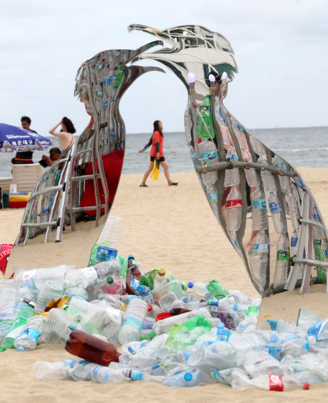 13일 부산 해운대구 해운대해수욕장에 일회용 플라스틱을 이용해 만든 미술작품 뒤로 피서객이 지나가고 있다. 그린피스는 이날부터 사흘간 해운대해수욕장에서 일회용 플라스틱으로 만들어진 미술작품을 통해 플라스틱 사용에 대한 경각심을 일깨우고 일회용 플라스틱 소비를 줄이는 방안에 대해 알릴 예정이다.  연합뉴스